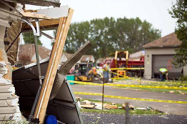 The image shows the aftermath of what appears to be structural damage to a building, with debris and wooden beams scattered around, yellow caution tape cordoning off the area, and emergency vehicles visible in the background.Retry